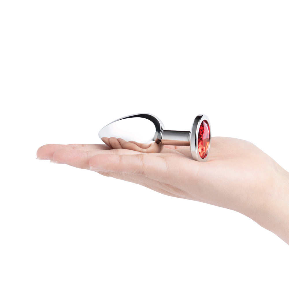 b-Vibe 3.25 Inch Stainless Steel Jewel Butt Plug Red held in a hand, showcasing its polished finish and red jewel base.
