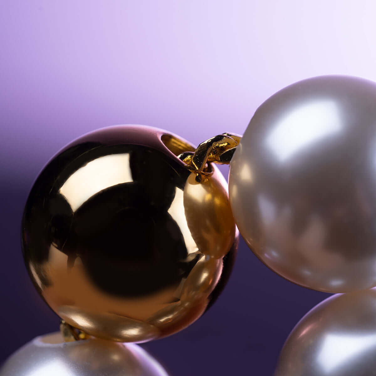 Close-up of UPKO "Moist Eyes" Pearl Anklet with gleaming pearls and gold link on a soft purple background.