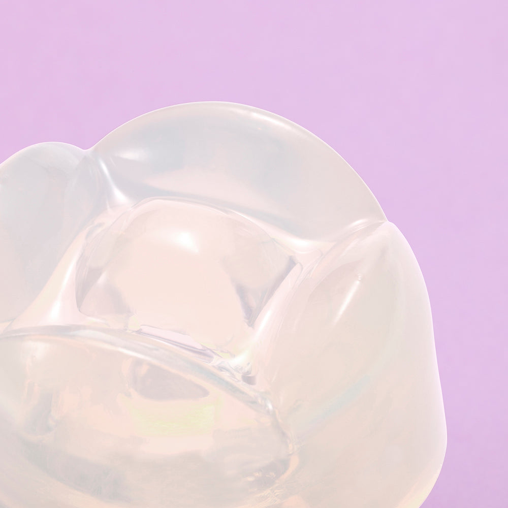Iroha Petit Lily Disposable Clitoral Massager Clear close-up on pink background highlighting its gel-like texture.