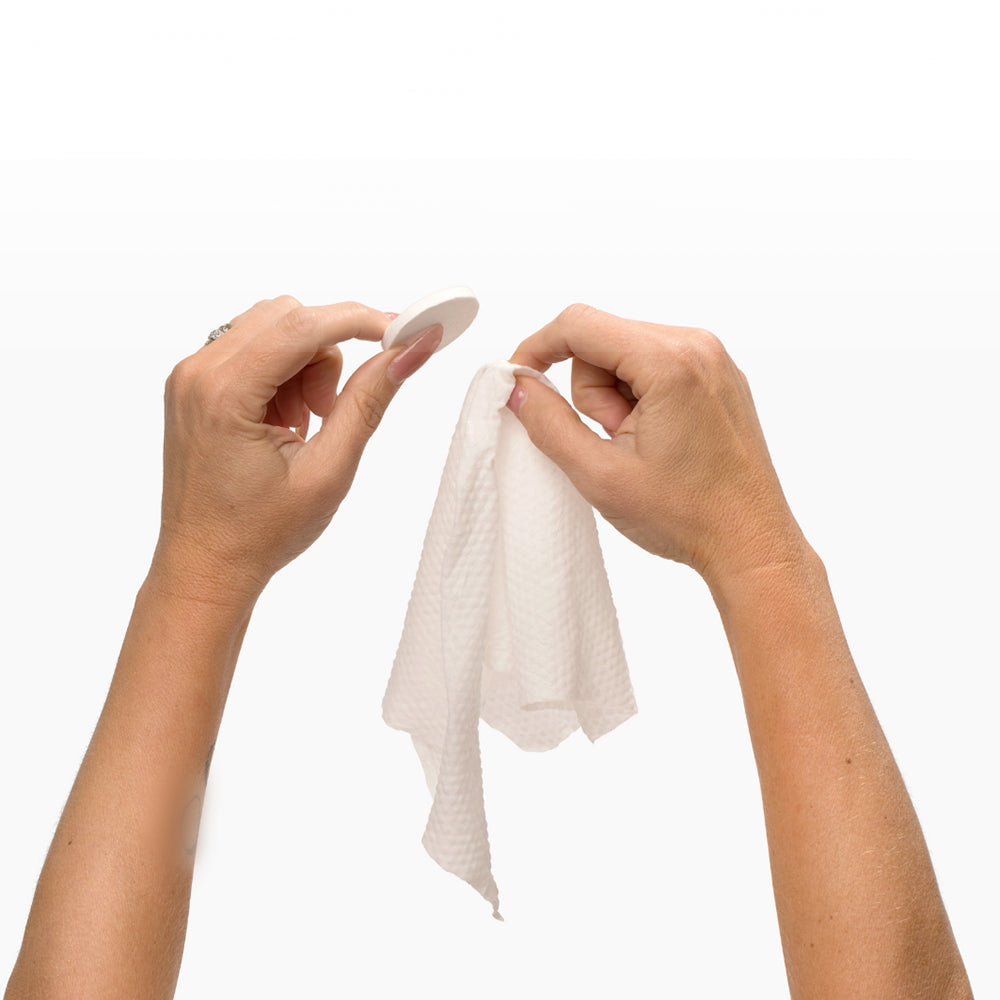 Hands holding a white towel and a circular pad, showcasing the Beloved Lovers Travel Kit essentials.