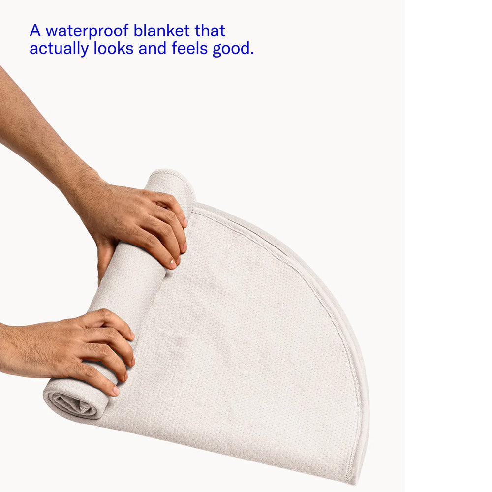 Dame Thro Waterproof Blanket for Play Oat being rolled up, showcasing its waterproof and soft design.