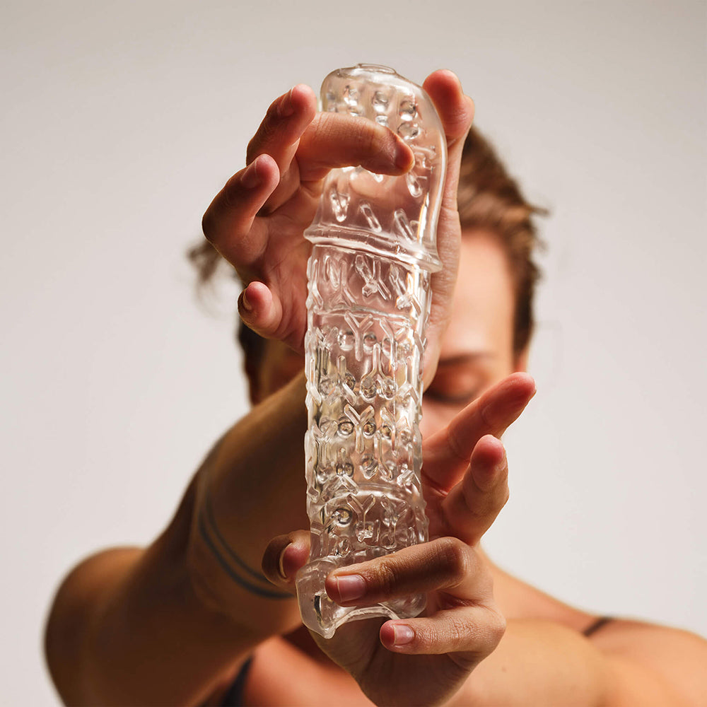 The Handy TrueGrip Gen 2 Masturbator Sleeve Clear held in hands, showcasing its textured design and clear material.