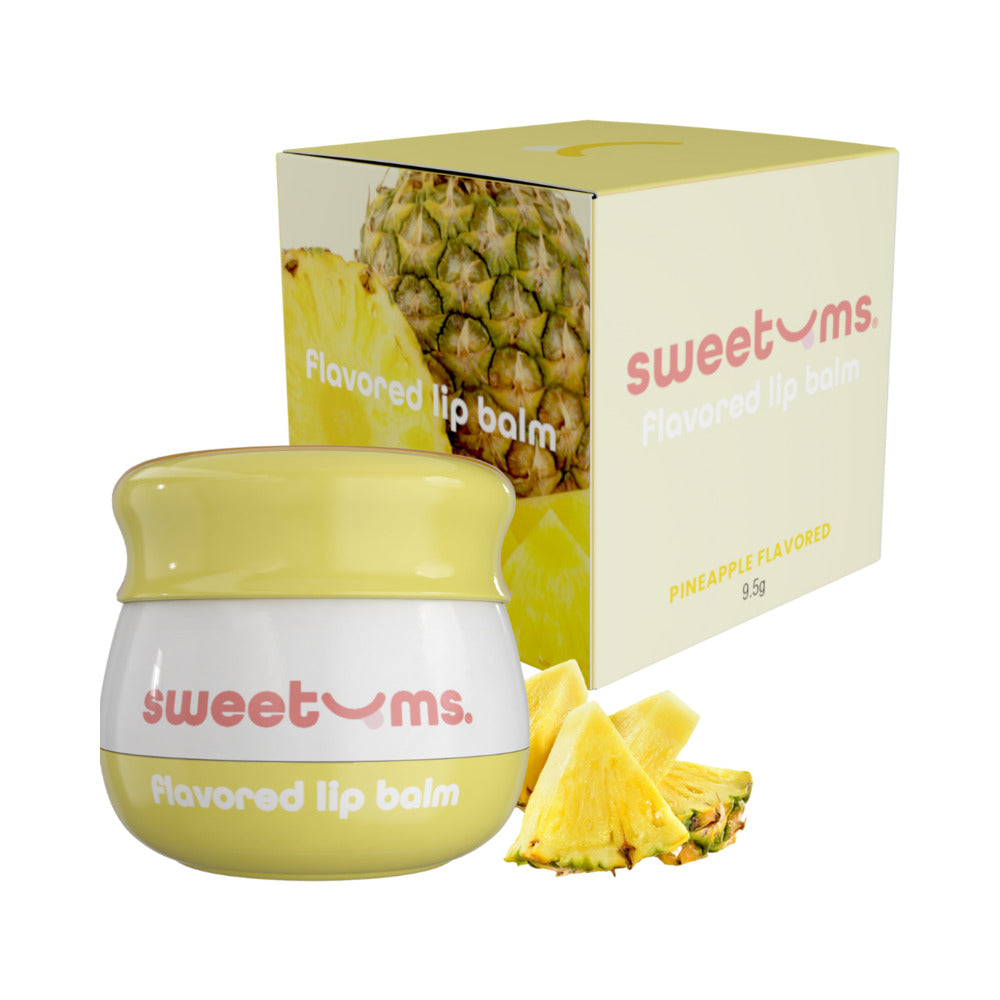 Sweetums Pineapple Flavored Lip Balm in a jar with a yellow lid, beside fresh pineapple pieces and packaging.