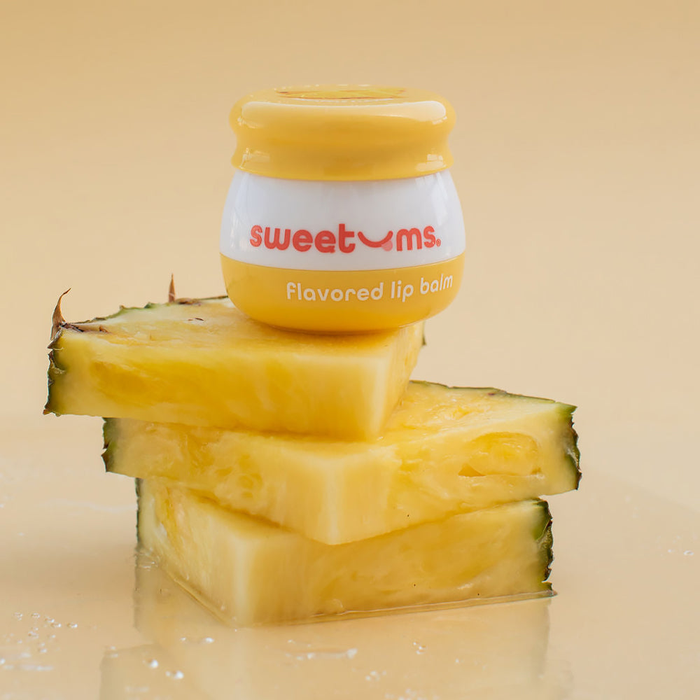 Sweetums Pineapple Flavored Lip Balm on pineapple slices, showcasing tropical flavor and hydration.