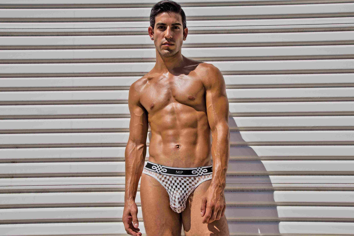 Male Power Peep Show Low Rise Thong White Small to Medium on a model posing confidently against a striped backdrop.