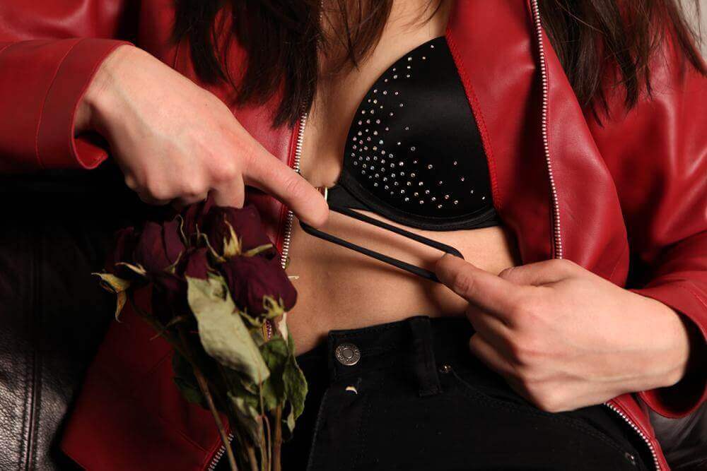 A person in a red jacket holding dried roses, playfully adjusting a black C-ring against their skin.