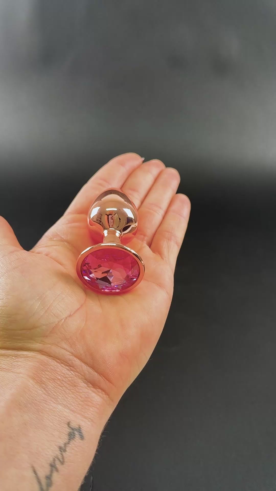 Camtoyz Cobalt Anal Plug Lucio held in a hand, showcasing its polished metal finish and decorative pink stone base.
